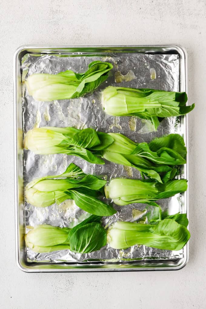 Baby bok choy halved and laid out cut side down on a foil lined baking sheet before being cooked.