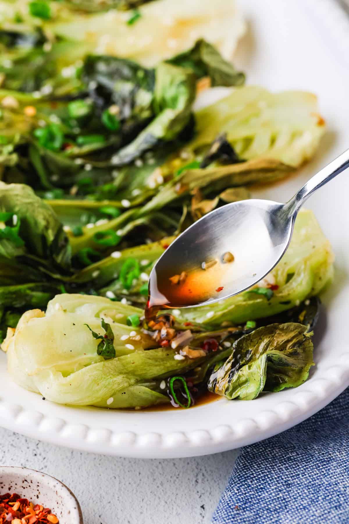 Honey garlic sauce being drizzled over roasted bok choy on a white serving platter.