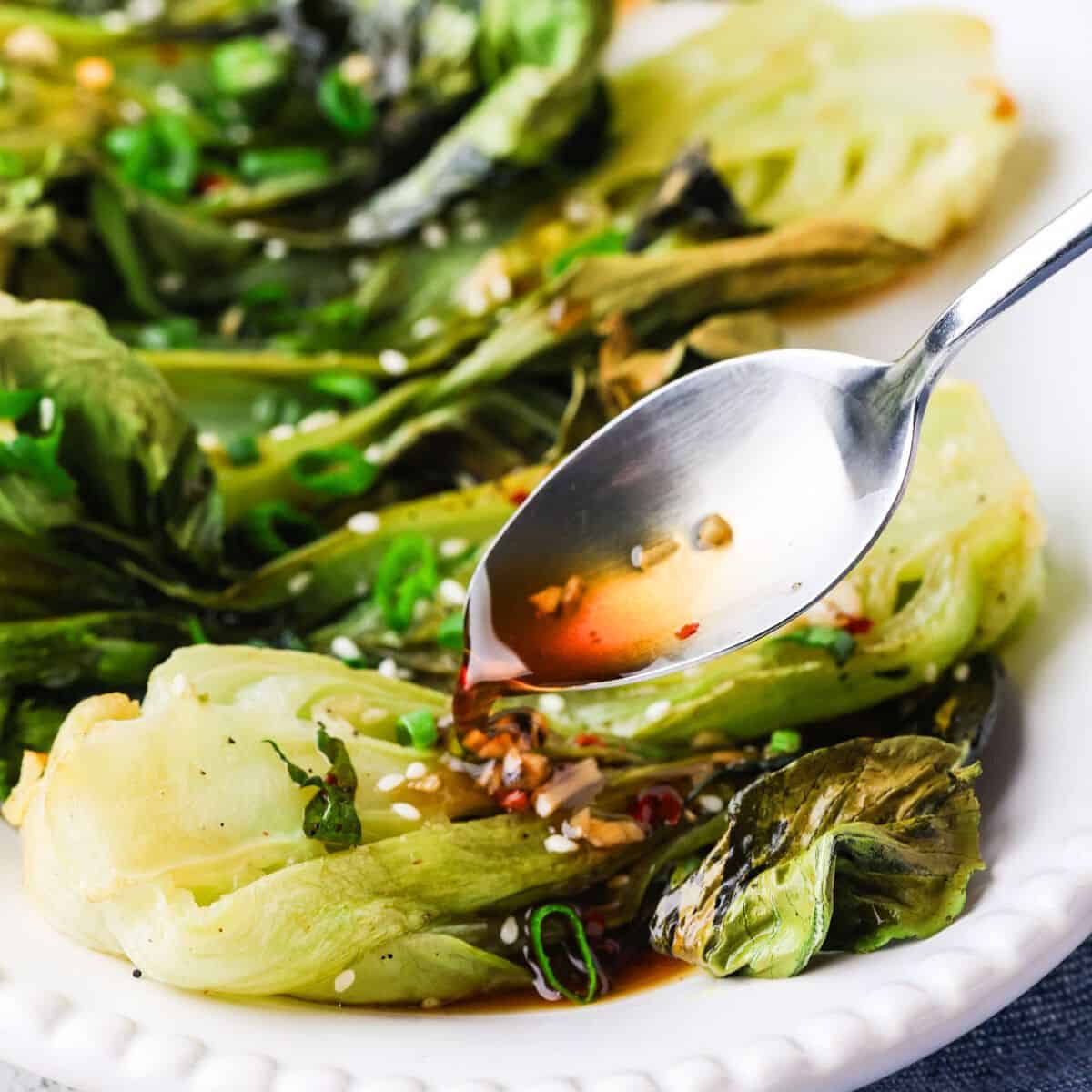 A spoon drizzling a honey garlic sauce over roasted bok choy on a serving platter.