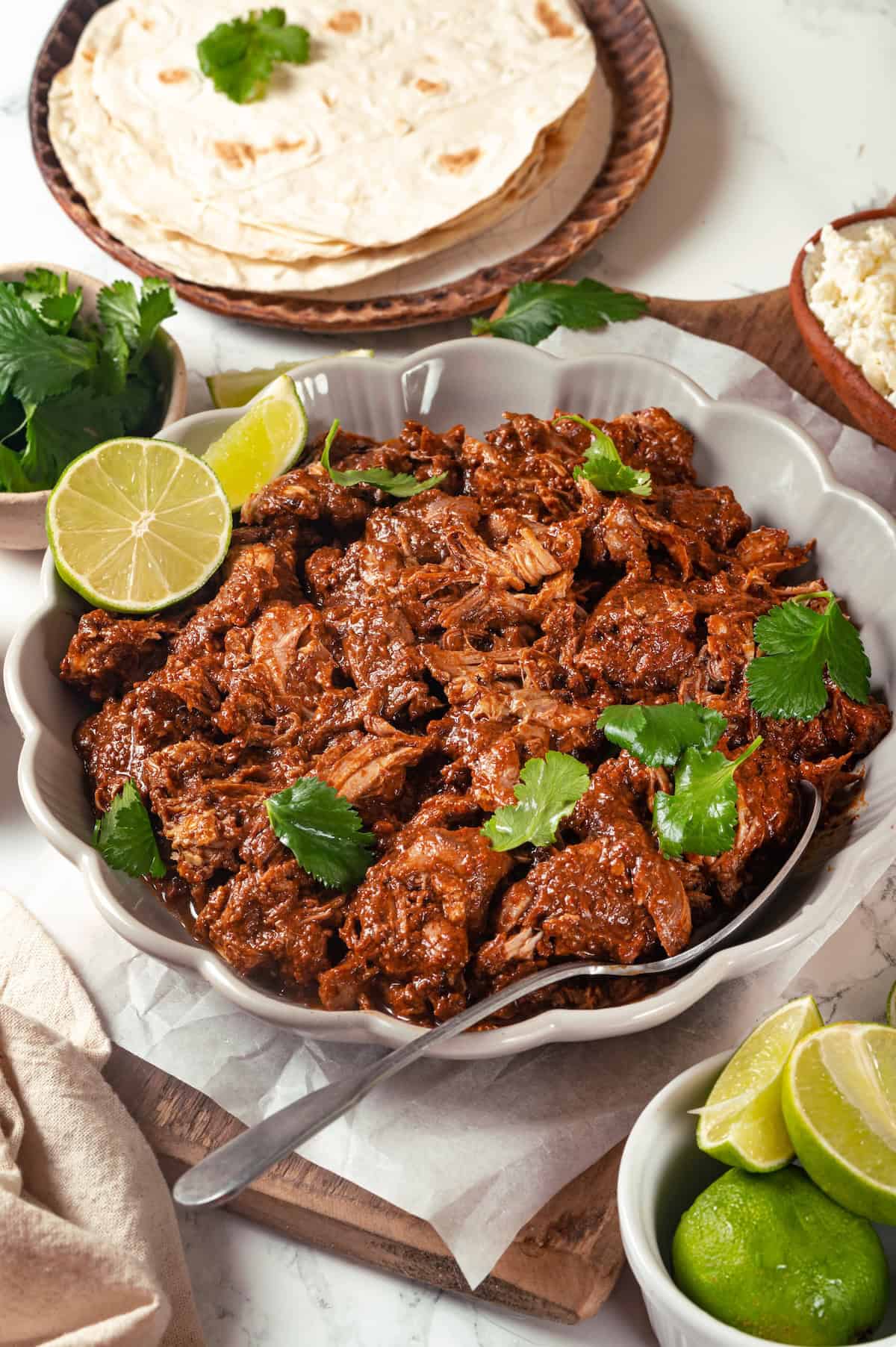Saucy mole chicken in a low serving bowl with cilantro and lime on top and a serving spoon to the side.
