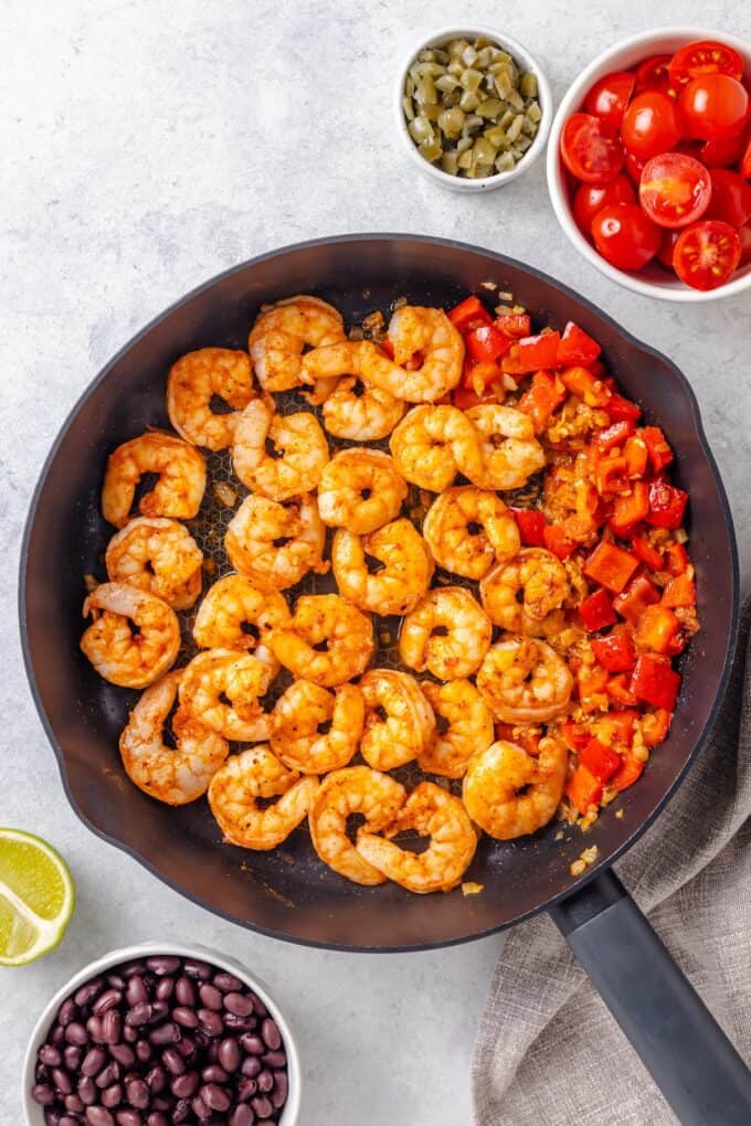 A large skillet with cooked shrimp alongside sautéed onion and red bell pepper.
