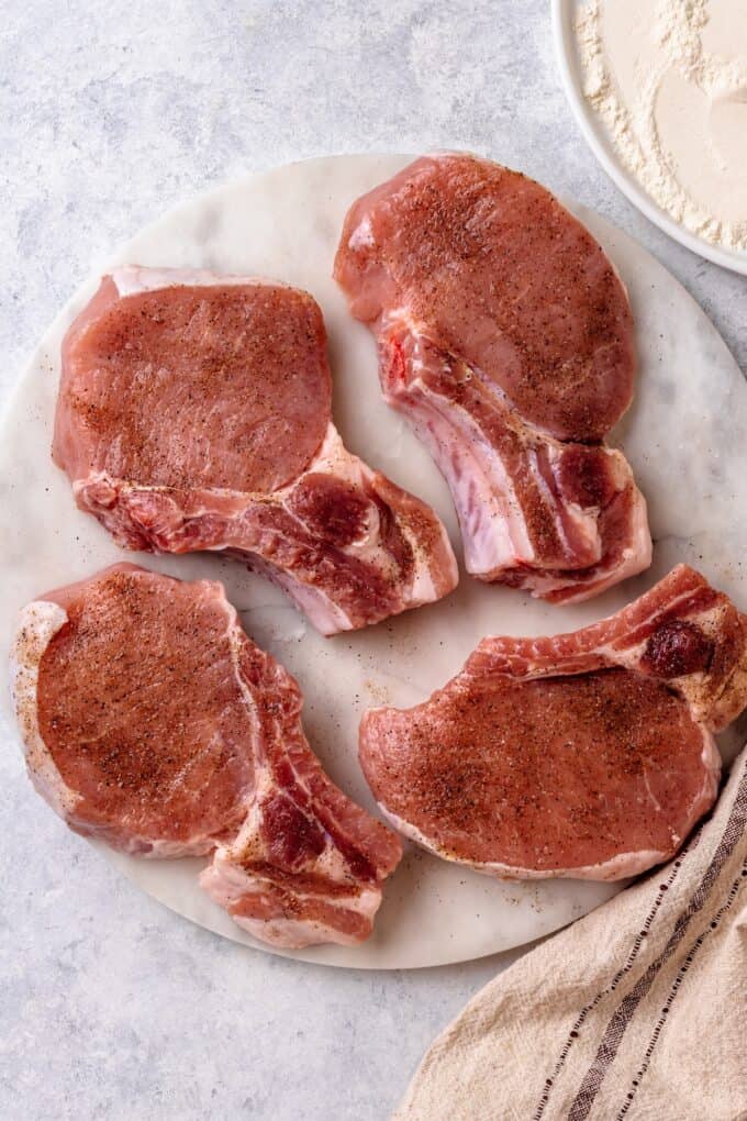 Seasoned bone in pork chops on a plate before being cooked.