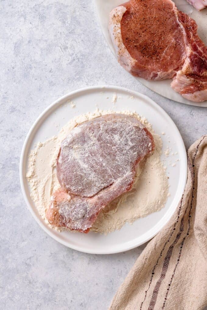 A pork chop being coated in flour before being cooked.