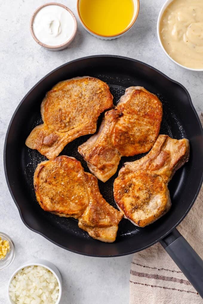 Seared pork chops with a golden crust in a cast iron pan.