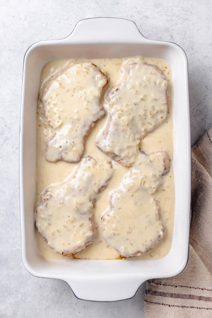Seared pork chops covered in gravy in a baking dish before being baked.