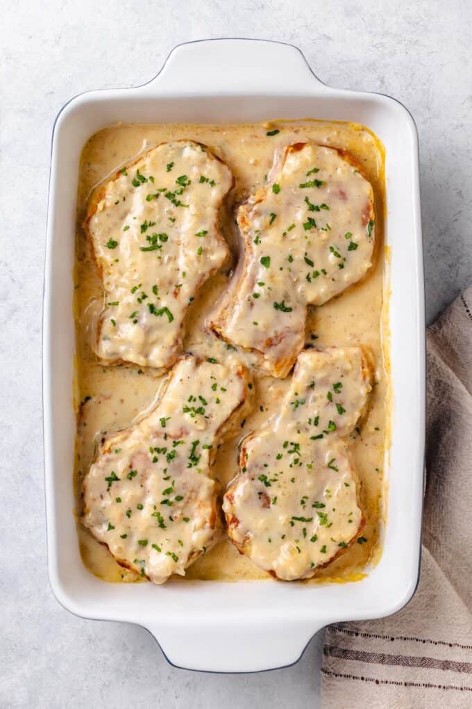 Baked pork chops in gravy in a baking dish with parsley sprinkled on top.