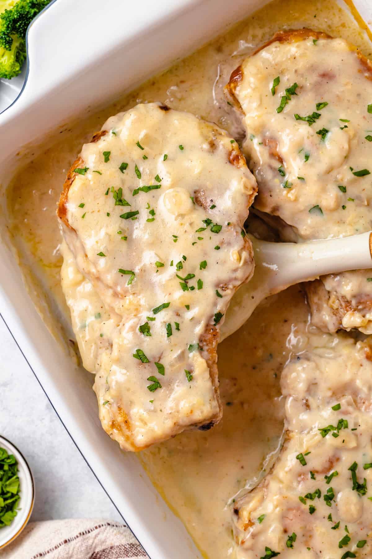 A baked pork chop with gravy being lifted out of a baking dish.