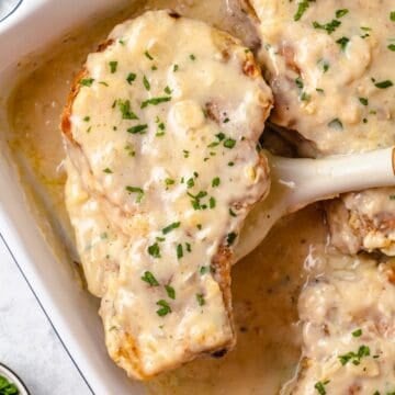 Close up of a baked pork chop with gravy being lifted out of a baking dish.