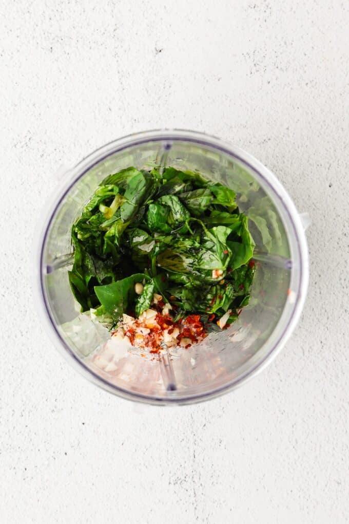 Basil and other vinaigrette ingredients in a blender cup before being combined.