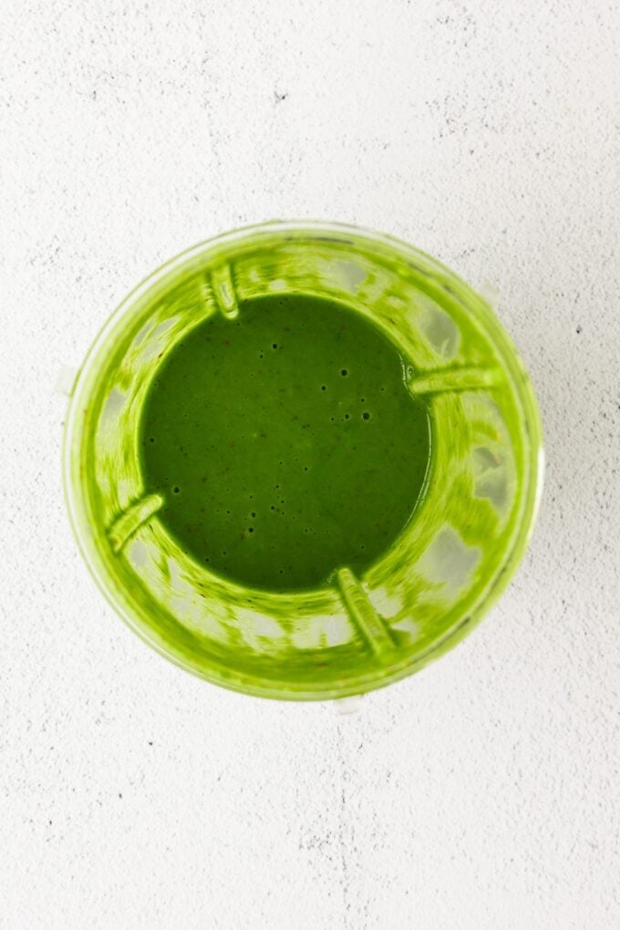 Bright green basil vinaigrette in a blender cup after being blended.