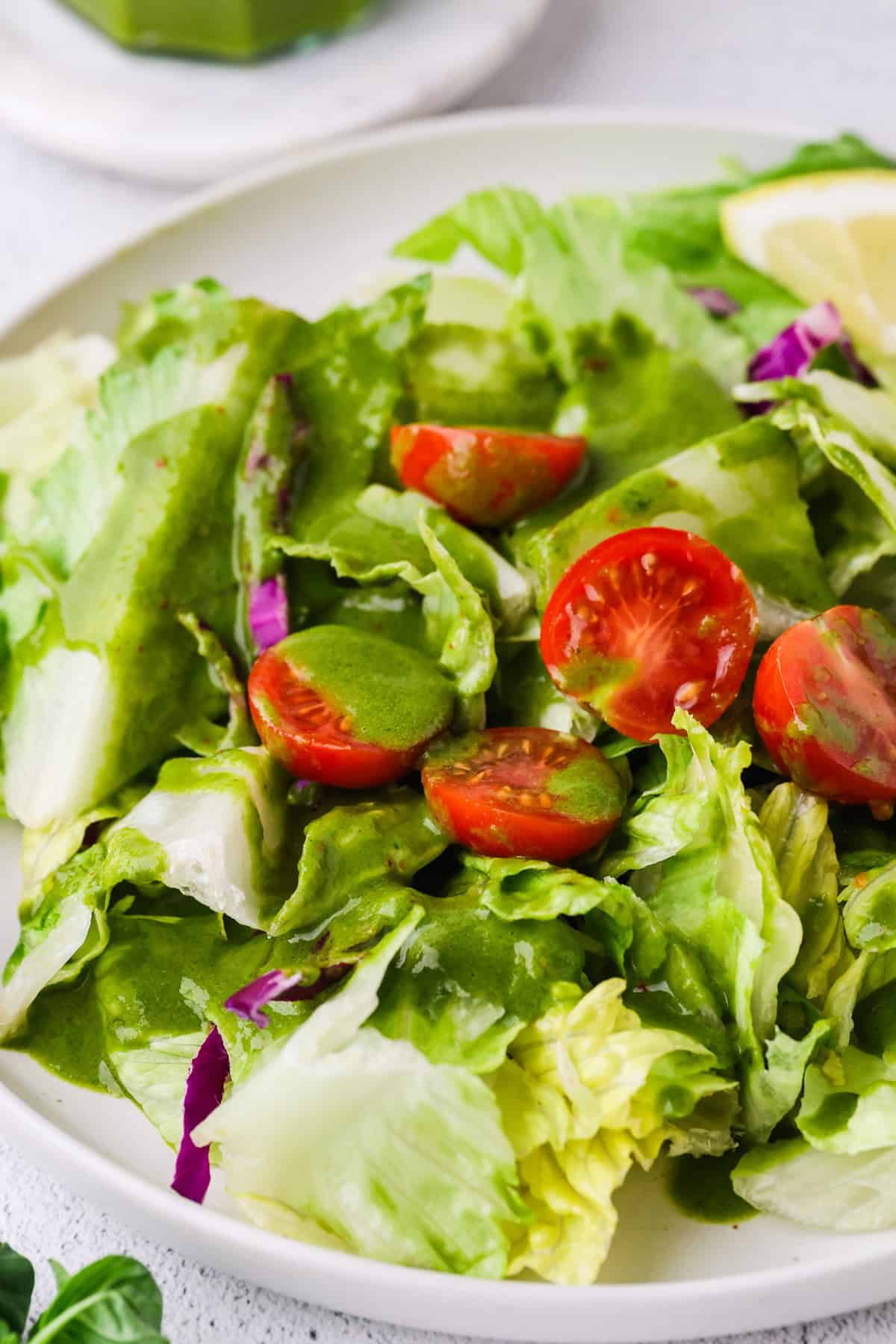 A mixed greens salad with tomatoes with a homemade basil dressing drizzled over top.