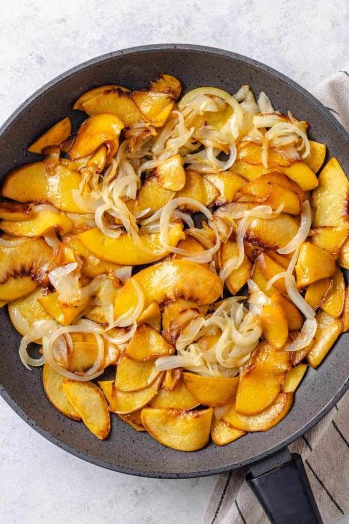Sautéed slices of onion and peaches in a skillet.