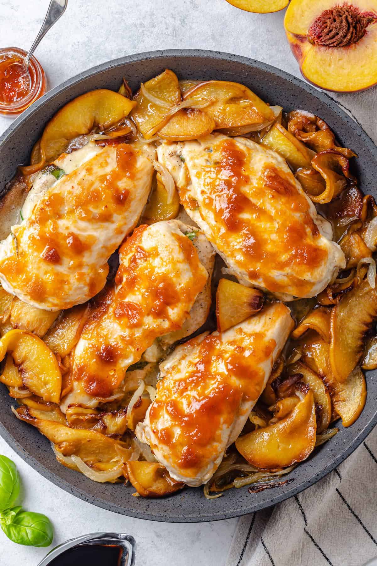 Brie cheese stuffed chicken breasts brushed with peach preserves in a skillet with sautéed slices of onion and peaches.