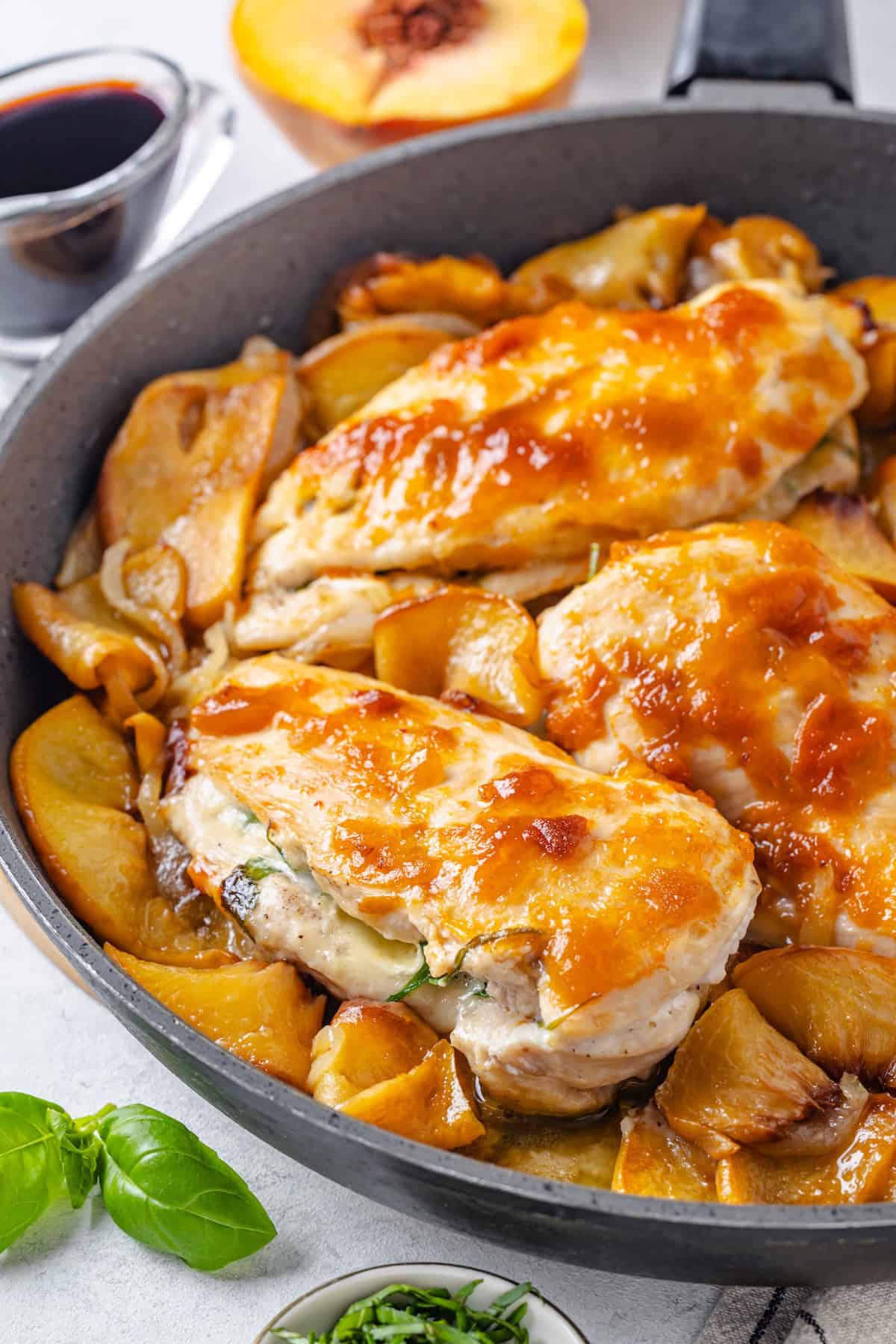 Close up of peach preserve brushed chicken breasts stuffed with brie cheese in a skillet with sautéed slices of onion and peaches.