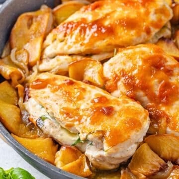 Close up of peach preserve topped chicken breasts stuffed with brie cheese in a skillet with sautéed slices of onion and peaches.