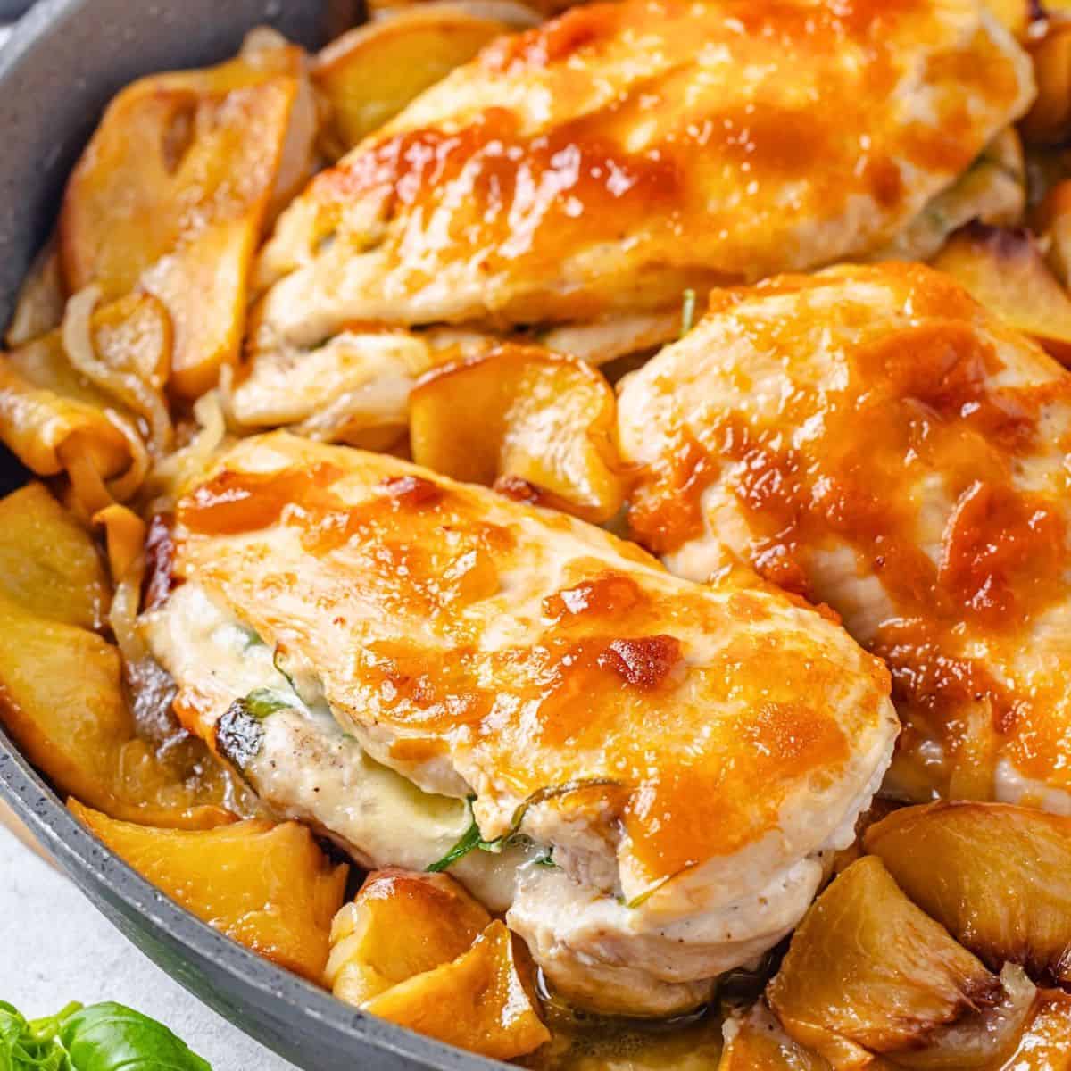 Close up of peach preserve topped chicken breasts stuffed with brie cheese in a skillet with sautéed slices of onion and peaches.