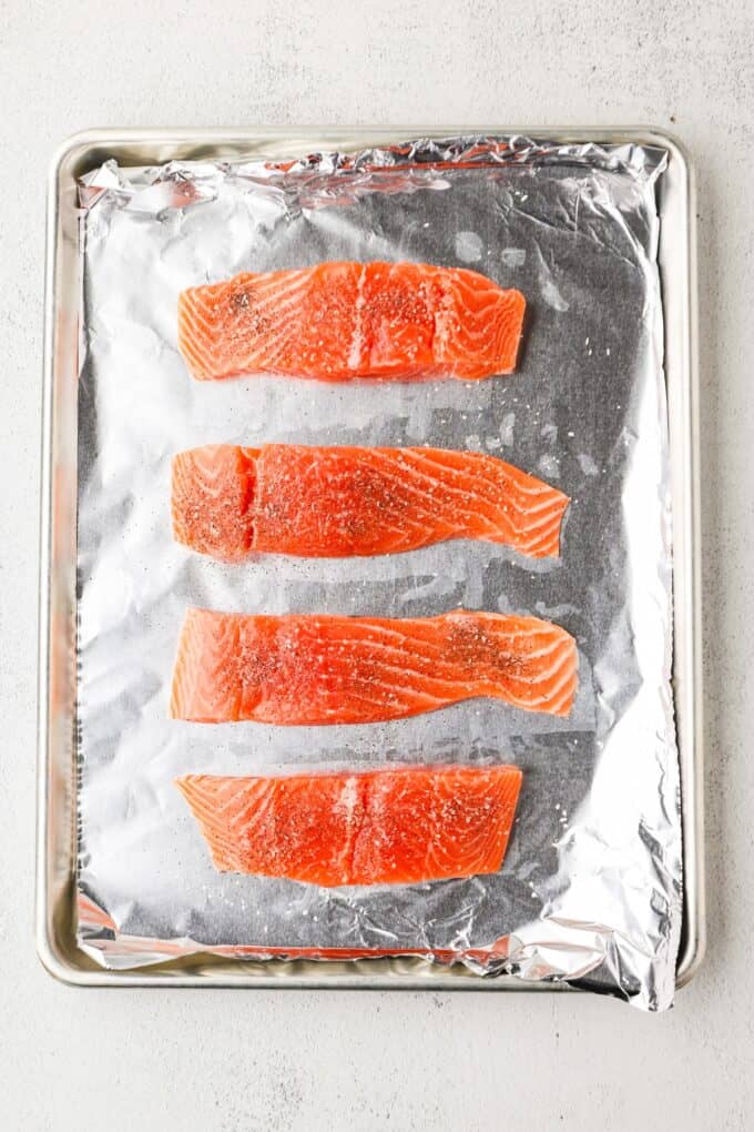 Seasoned salmon filets on a foil lined baking sheet.
