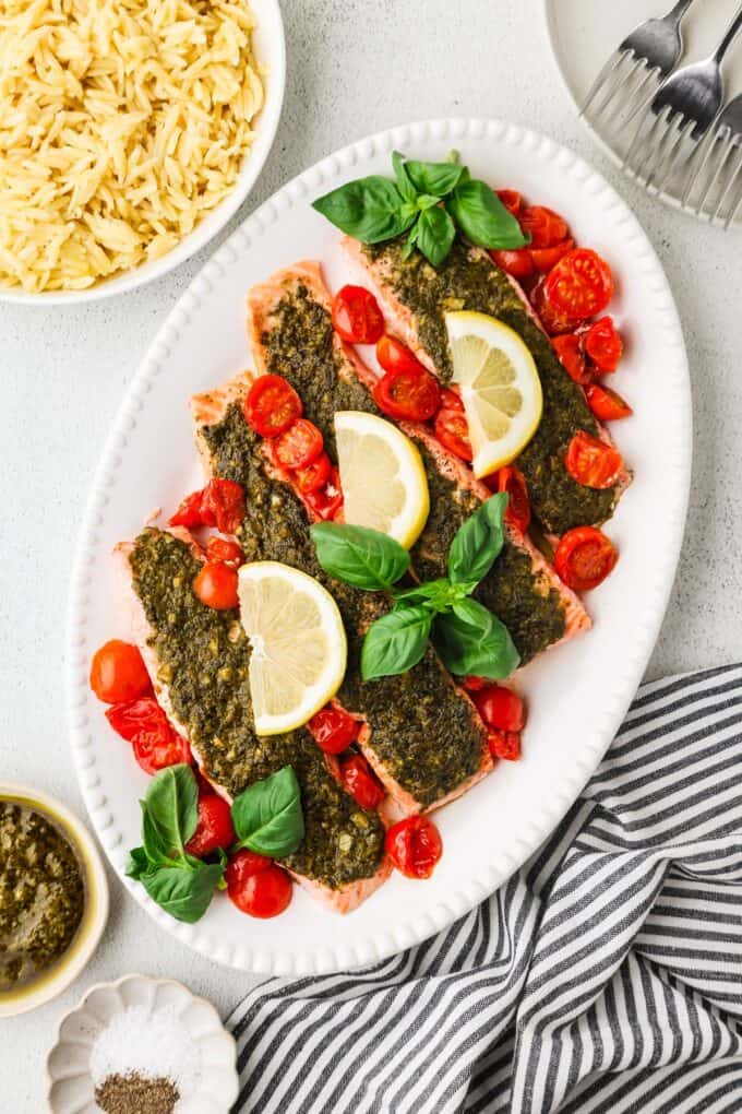 Broiled pesto salmon in a serving dish alongside a bowl of orzo.