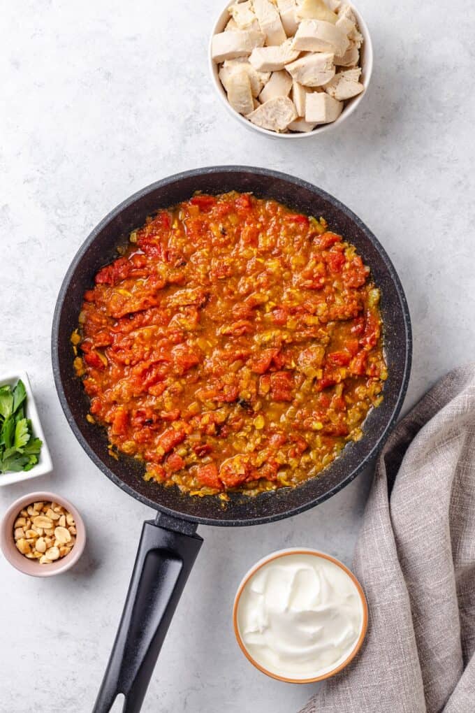A homemade tomato curry sauce being layered into a skillet.