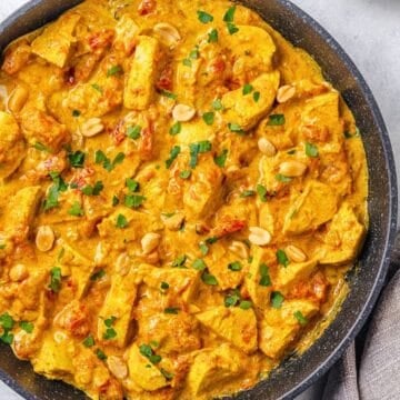 Close up of an easy one pan chicken curry in a large skillet with peanuts and cilantro sprinkled on top.