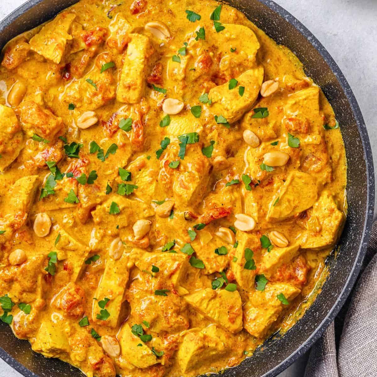 Close up of an easy one pan chicken curry in a large skillet with peanuts and cilantro sprinkled on top.