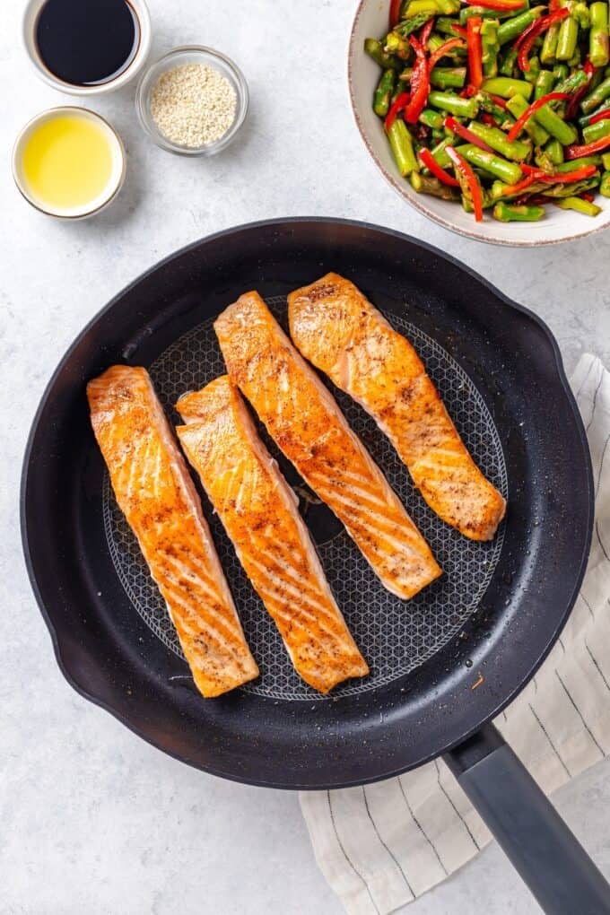Four seared thin salmon filets in a large dark skillet.