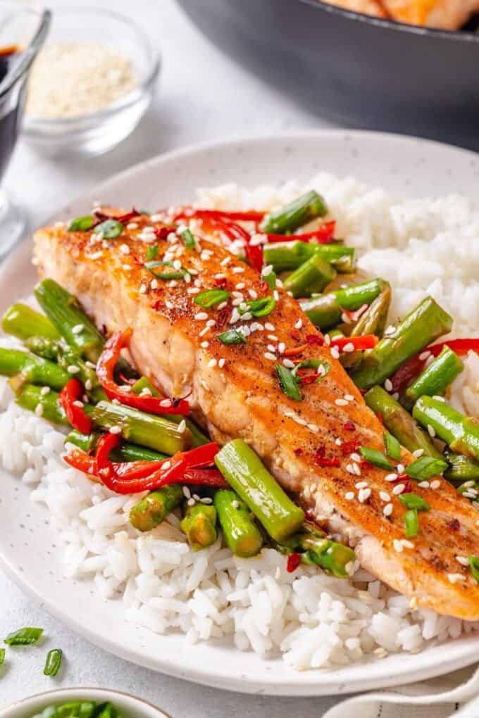 A long, skinny salmon filet with asparagus and red pepper on a bed of white rice on a dinner plate.
