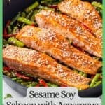 Close up of seared salmon filets in a large dark skillet on a bed of asparagus and red bell pepper pieces with a green border and text box around the photo.