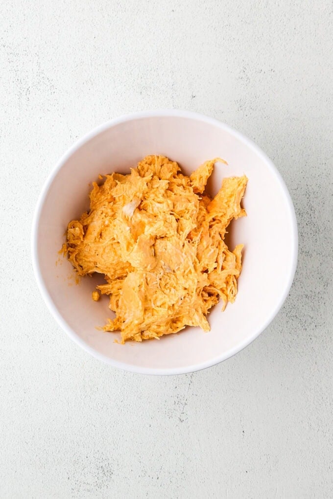 A creamy shredded chicken mixture with buffalo sauce in a white bowl.