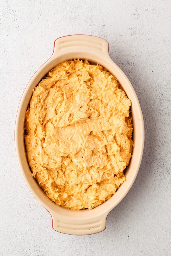 A creamy buffalo chicken dip mixture spread out into a baking dish.