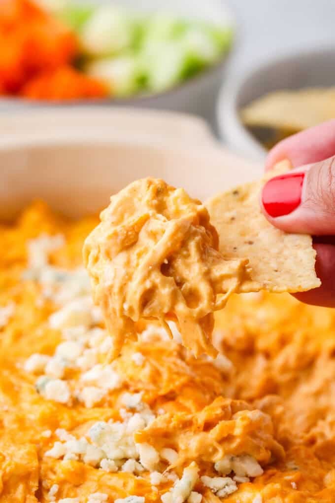 A hand lifting up a chip with buffalo chicken dip on it from a casserole dish.