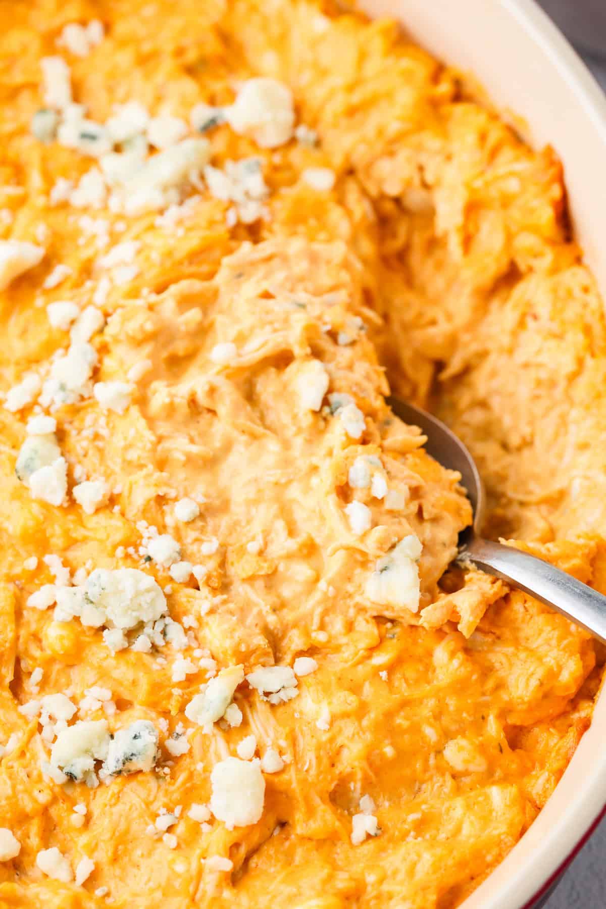 A spoon resting in a baking dish with a creamy buffalo chicken dip appetizer topped with blue cheese crumbles.