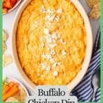A baked buffalo chicken dip with blue cheese crumbles on top and chips and veggie sticks nearby for dipping with a green border and text around the photo.