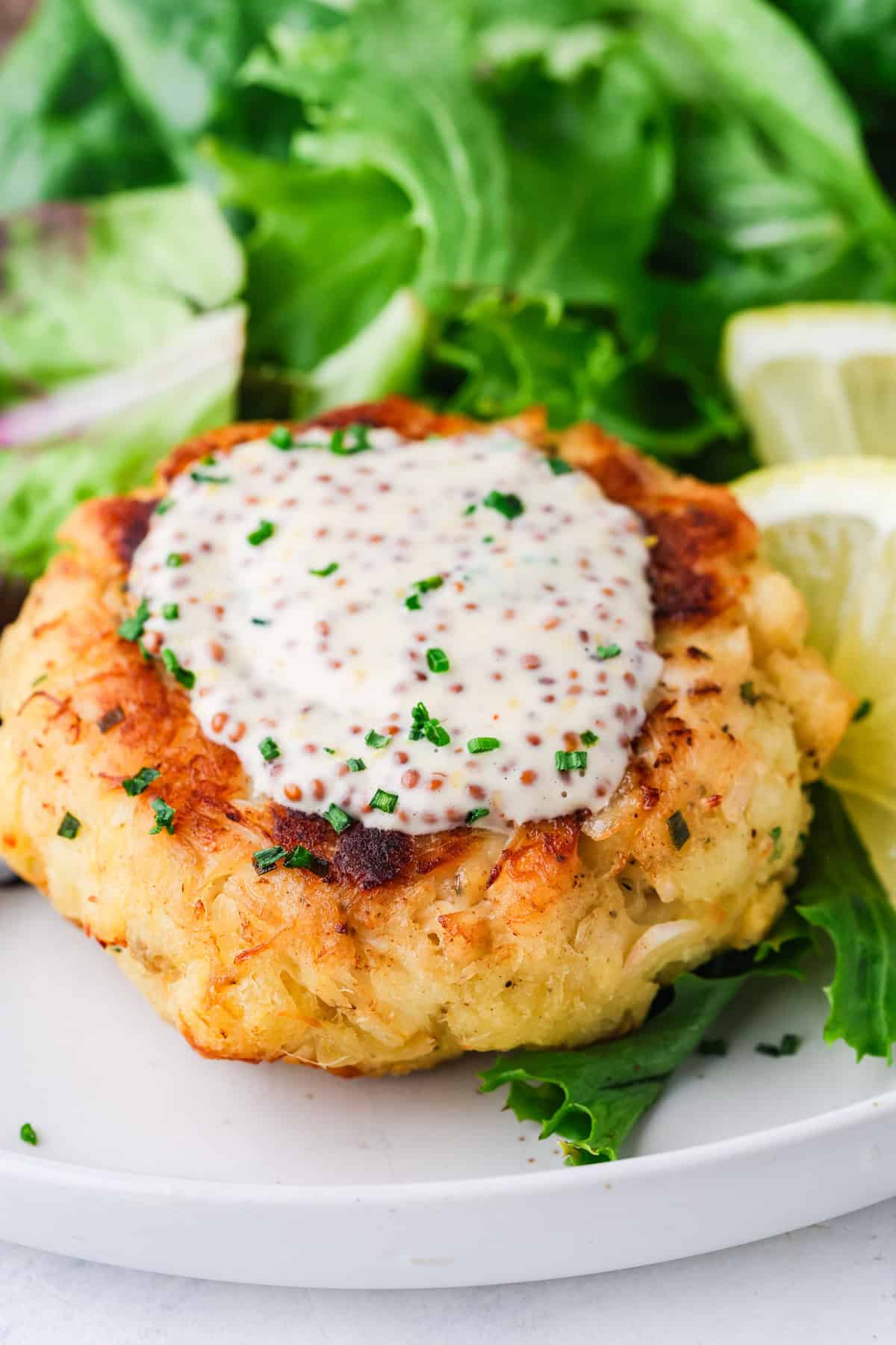 Close up of a crab cake with mustard remoulade on top sprinkled with finely chopped chives.