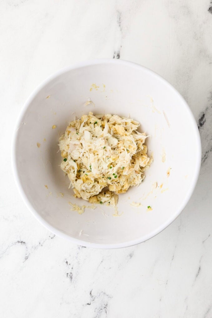 Jumbo lump crab meat being mixed with seasonings in a small white bowl.