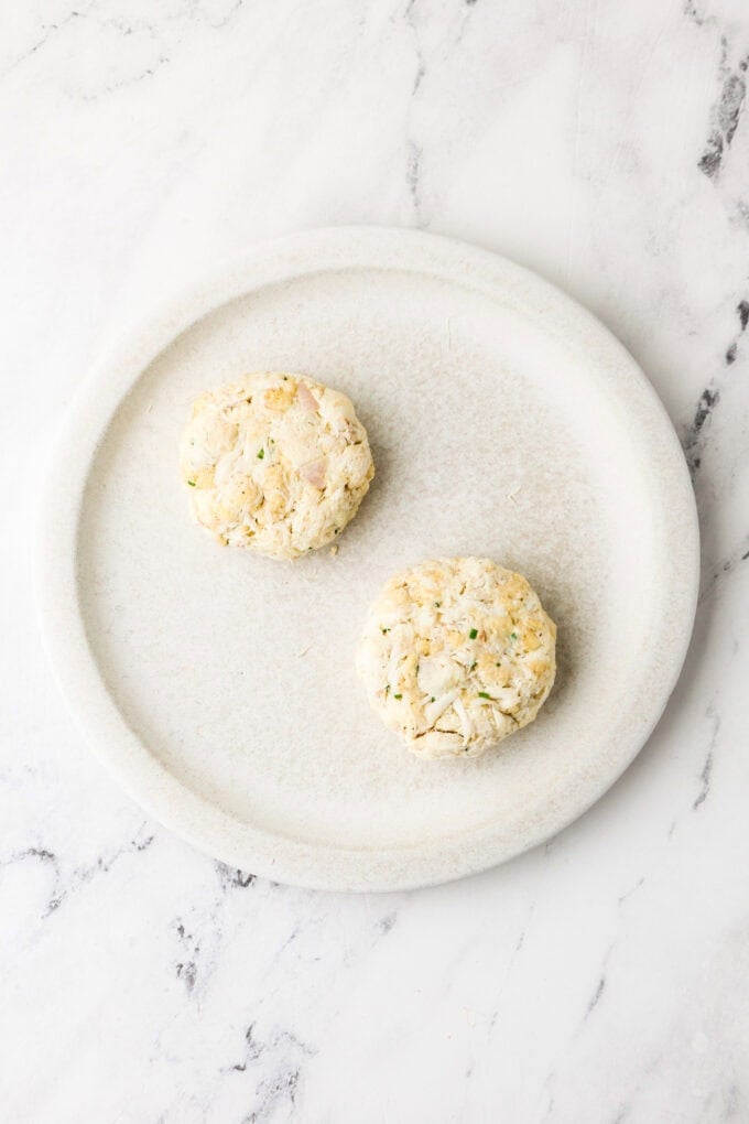 Two small jumbo lump crab cakes on a plate before being cooked.