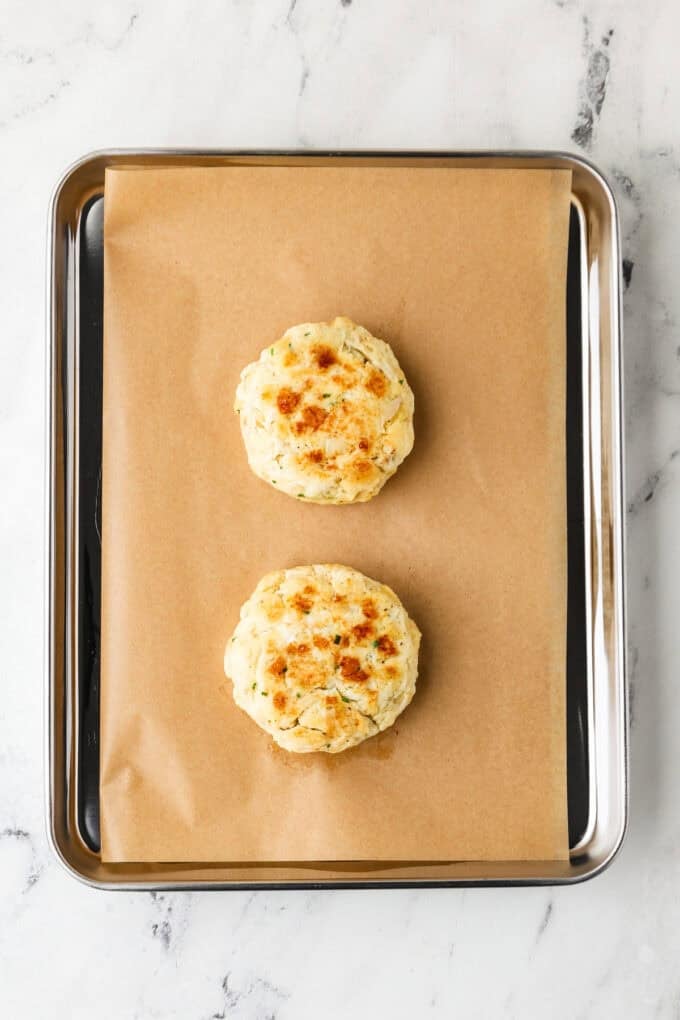 Two seared crab cakes on a baking sheet before being baked in the oven.
