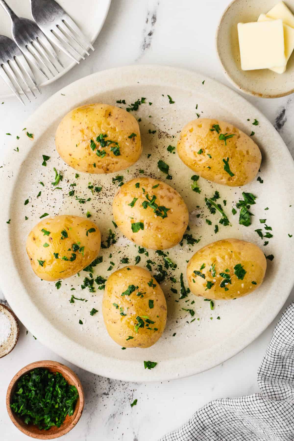 A plate full of cooked Yukon potatoes with butter, salt and parsley on top.