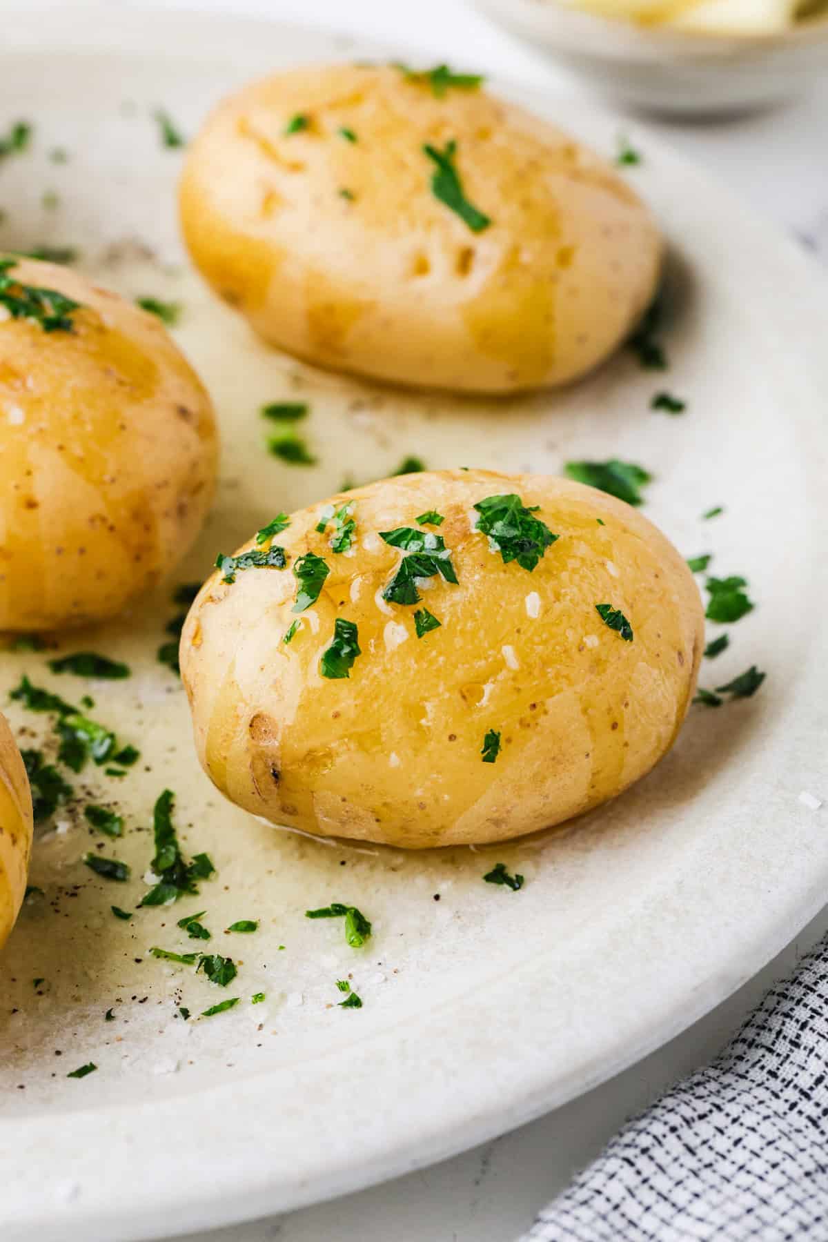 Close up of microwave baked Yukon potatoes on a plate with melted butter drizzled over and some salt and parsley sprinkled on top.