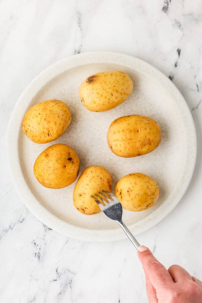 Yukon gold potatoes on a plate and being pierced with a fork.
