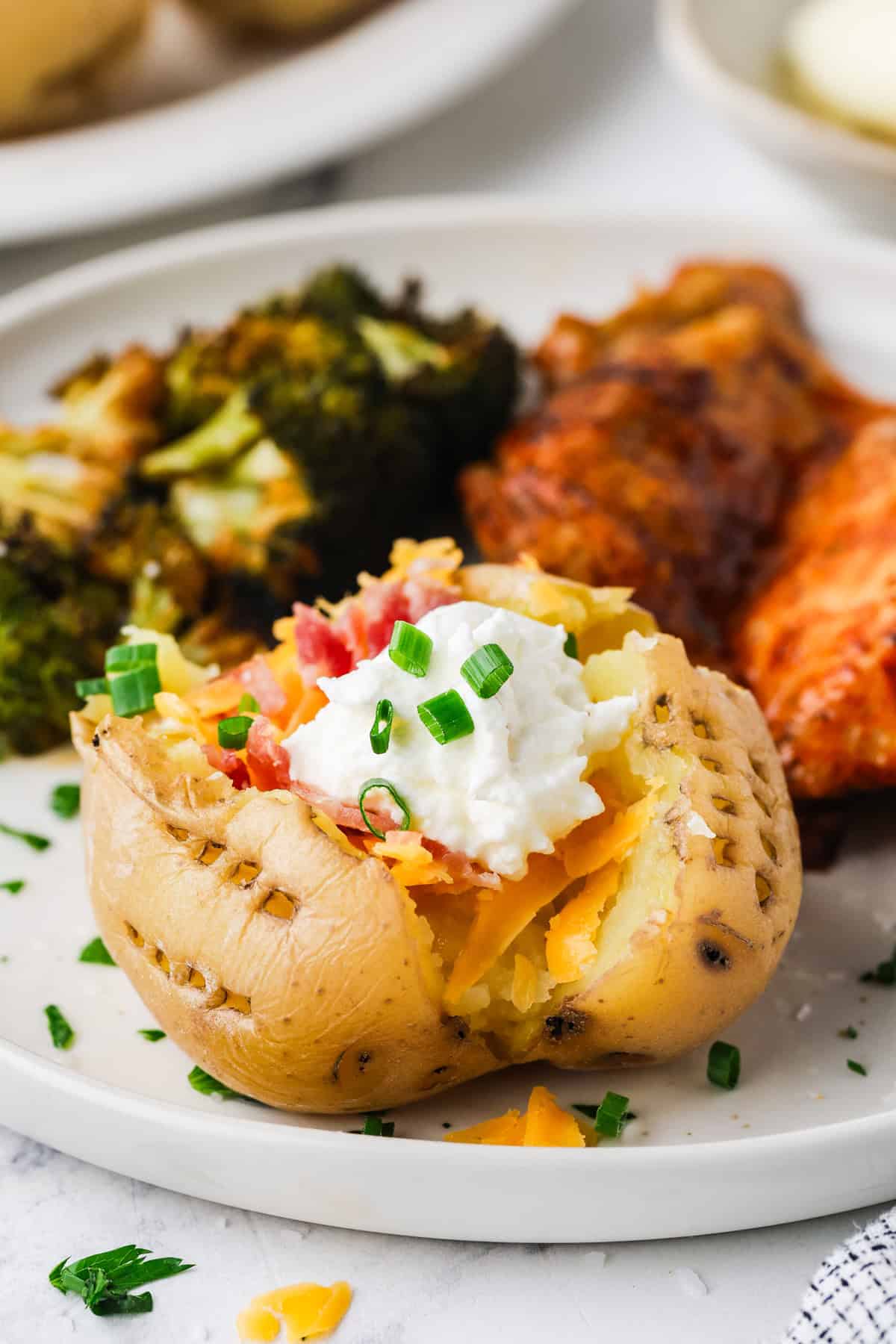 A loaded Yukon potato on a plate with cheese, bacon, chives and sour cream as toppings.