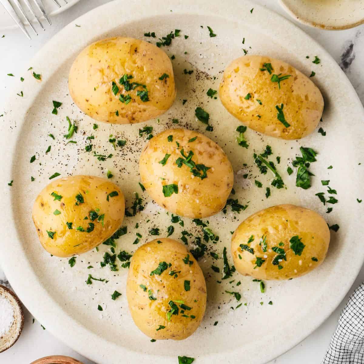 Close up of a plate full of cooked Yukon potatoes with butter, salt and parsley on top.