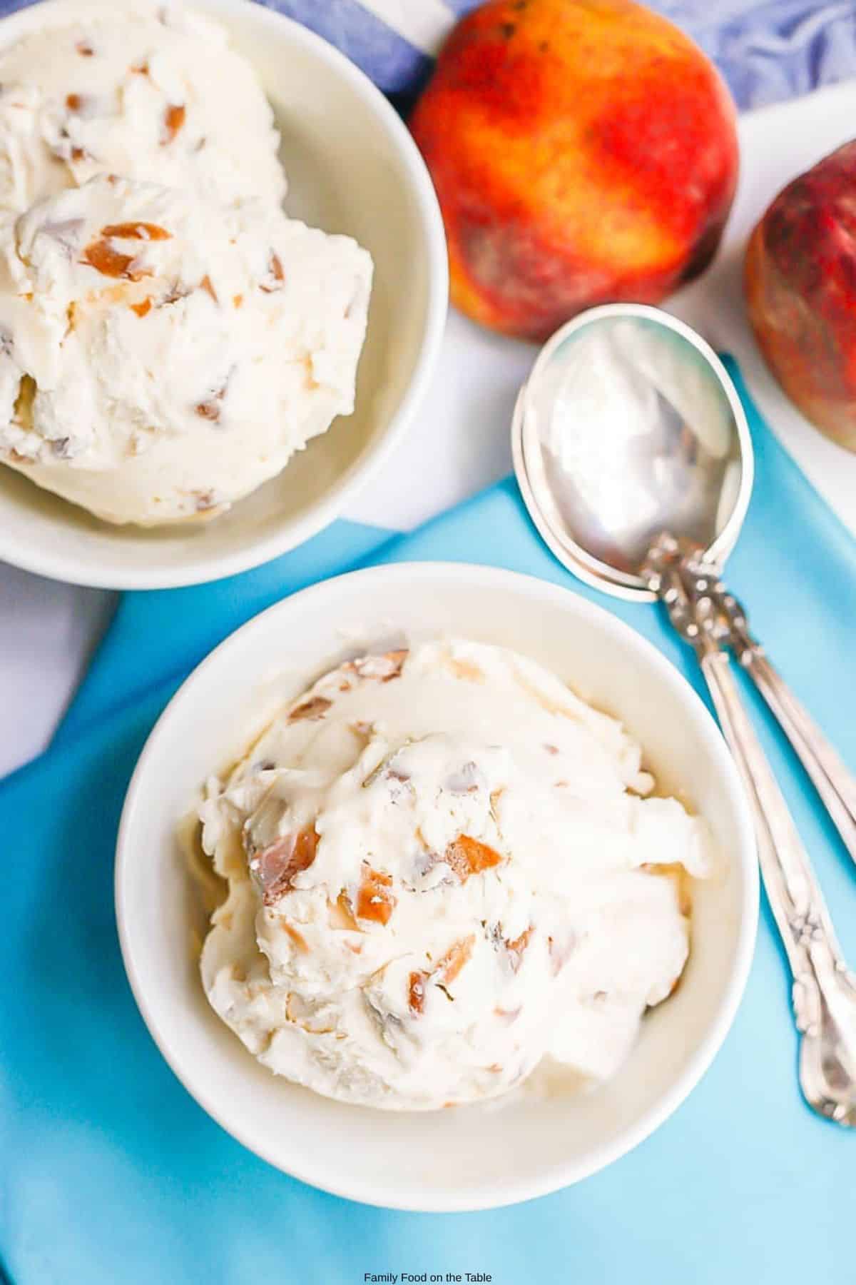 A small white bowl of homemade no churn peach ice cream set on a teal napkin with spoons to the side.