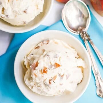 Close up of a small white bowl of homemade no churn peach ice cream set on a teal napkin with spoons to the side.