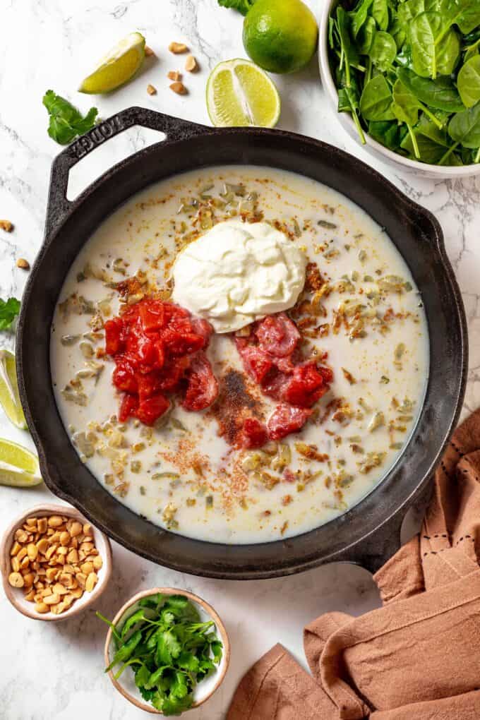 A milky sauce in a cast iron pan with dollops of Greek yogurt and tomatoes before being mixed in.