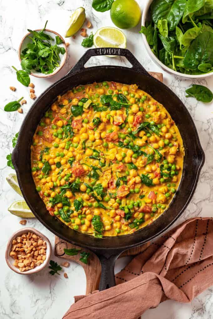 A vegetarian chickpea curry with spinach, tomatoes and peas in a cast iron pan.