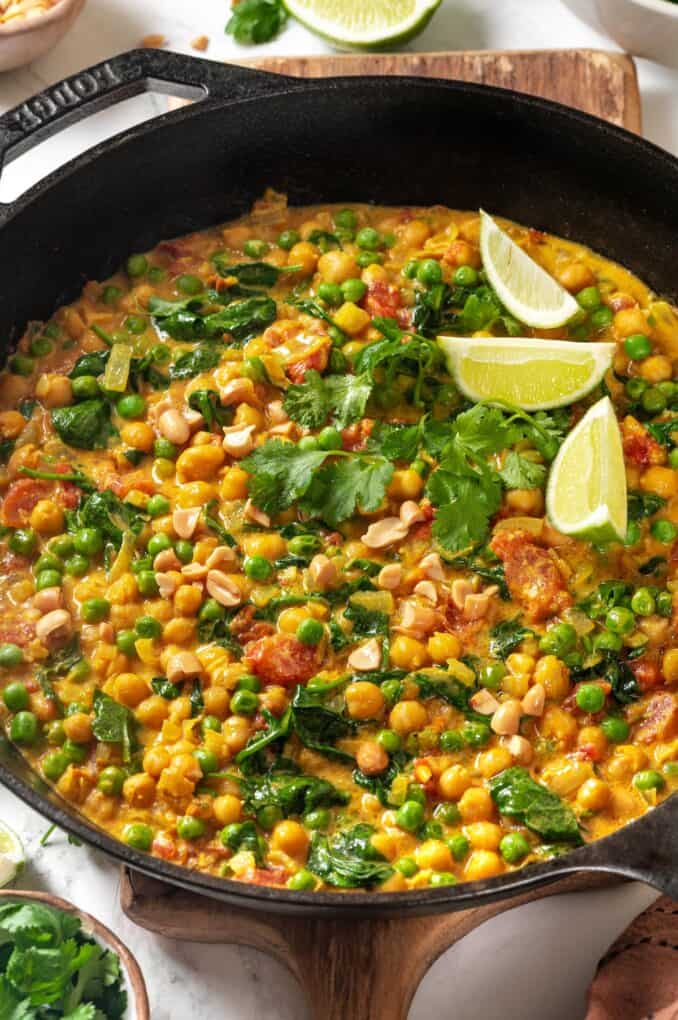 A homemade vegetarian curry in a cast iron pan with some cilantro leaves and lime wedges for garnish.