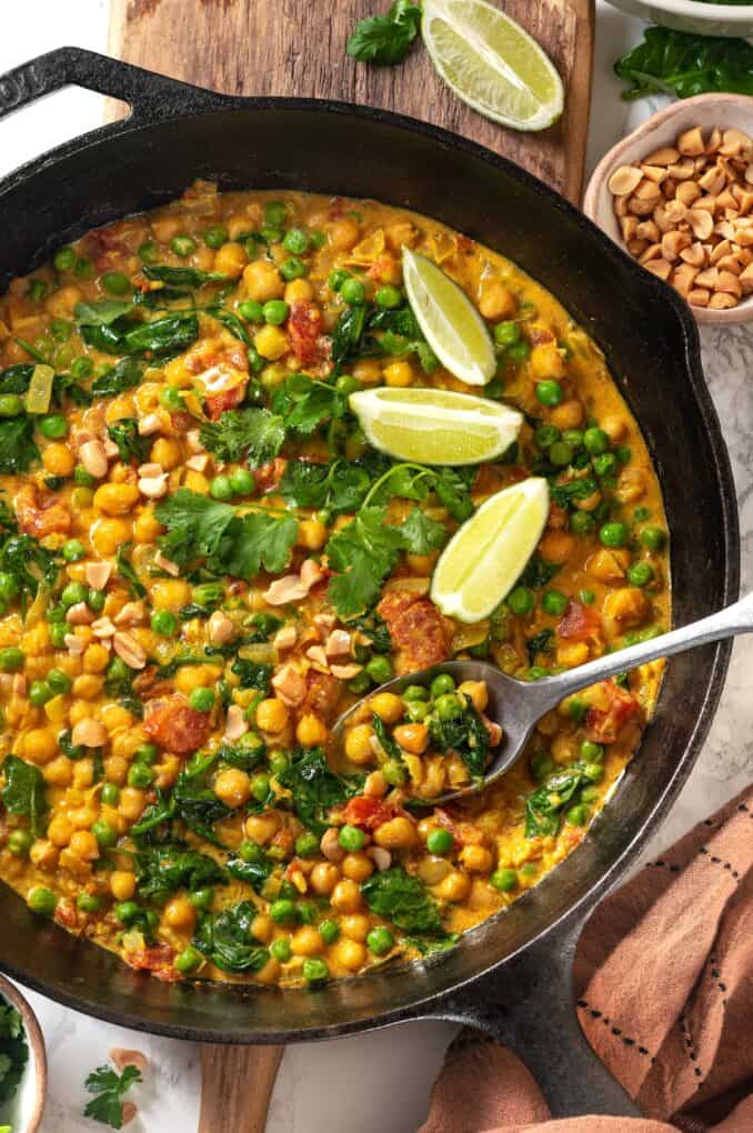 A spoon resting in a cast iron skillet with a chickpea curry with spinach, tomatoes and green peas.