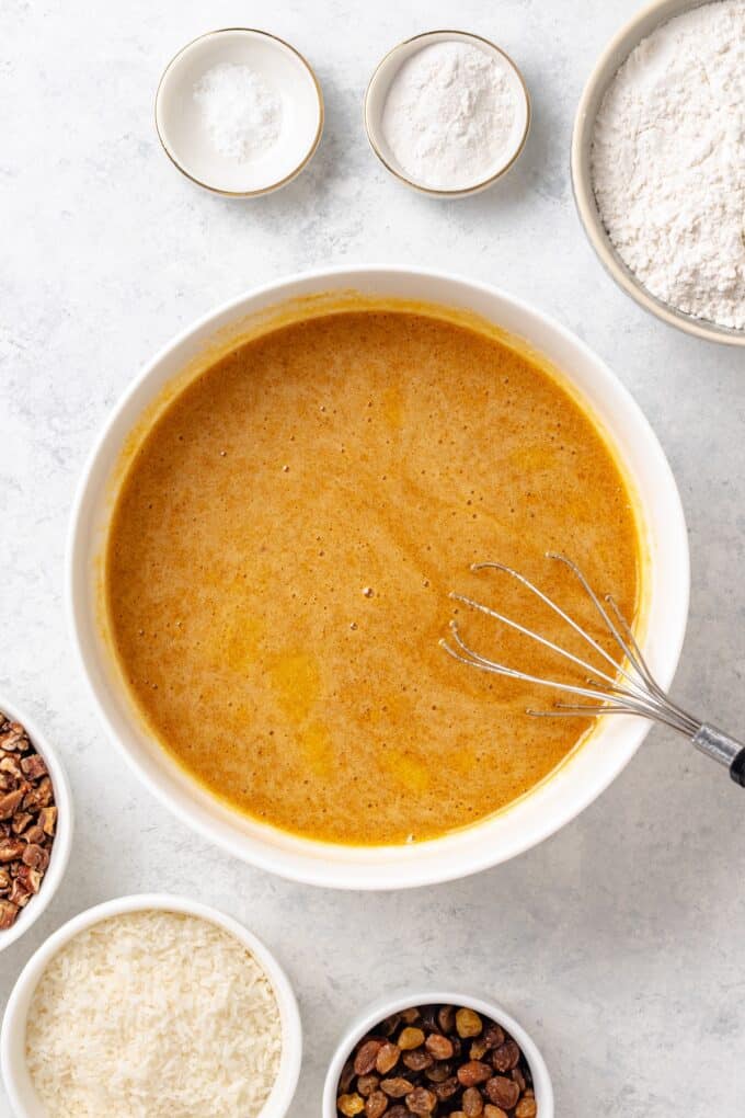 A white mixing bowl with a brown sugar and butter mixture being whisked together.