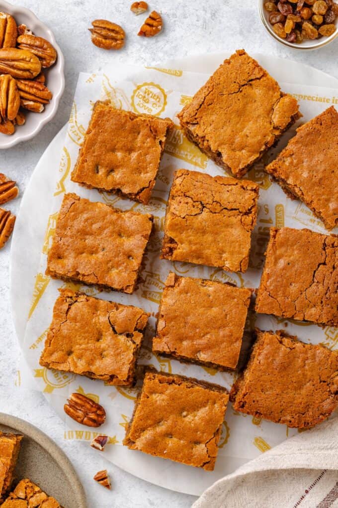 Cut squares of chew bread with pecans, raisins and coconut served on a white plate.